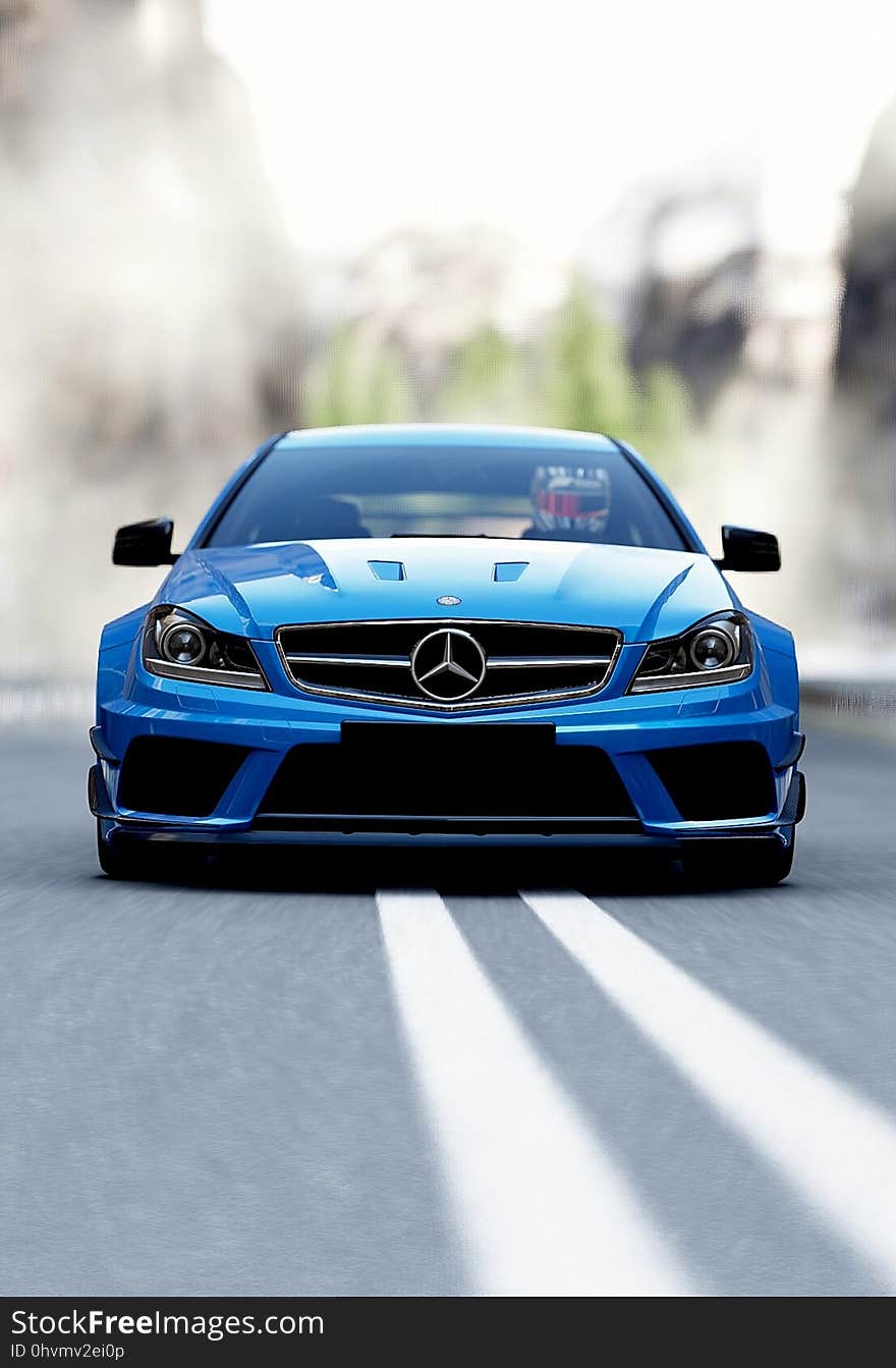 Front of blue Mercedes Benz large luxury saloon approaching along two white road markings, blurred background. Front of blue Mercedes Benz large luxury saloon approaching along two white road markings, blurred background.