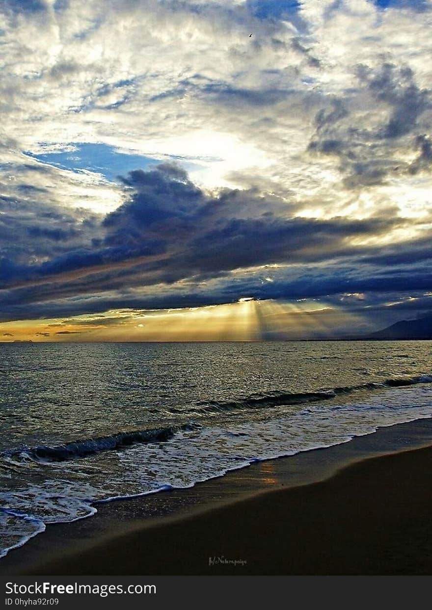 Tide coming in on the seashore at sunset with golden light and high fluffy clouds.