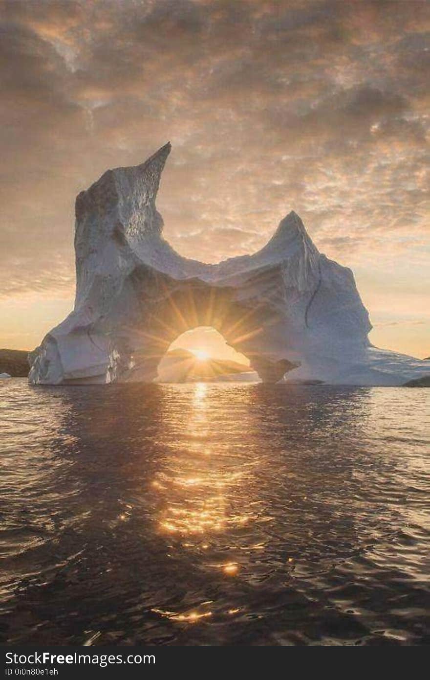 An iceberg and sunbeams glittering on the sea surface at sunset. An iceberg and sunbeams glittering on the sea surface at sunset.