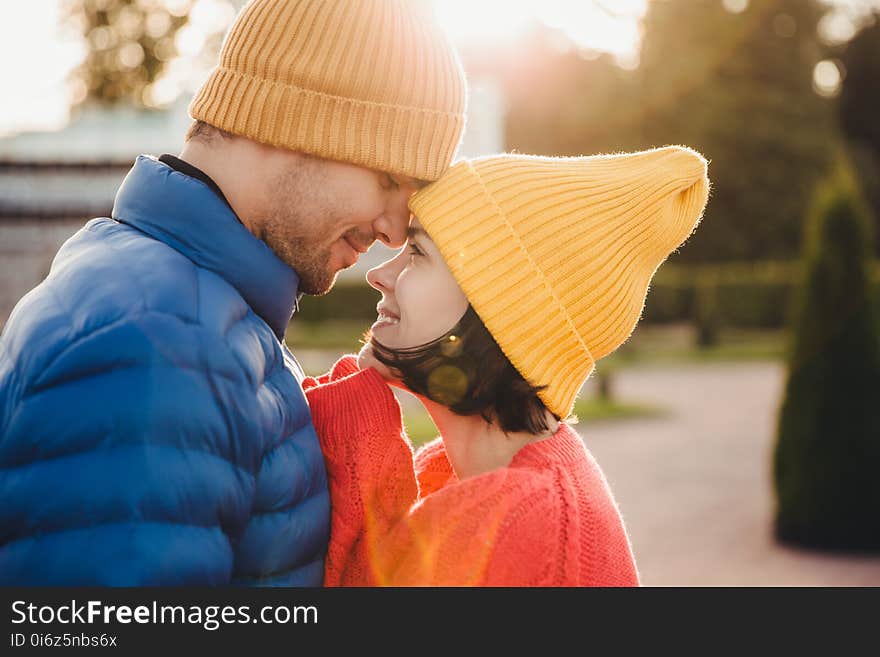 Romantic young couple look at each other with great love, have nice relationship, going to kiss, have walk outdoor in park, wear warm clothes. Lovely couple with eyes full of love and smile.