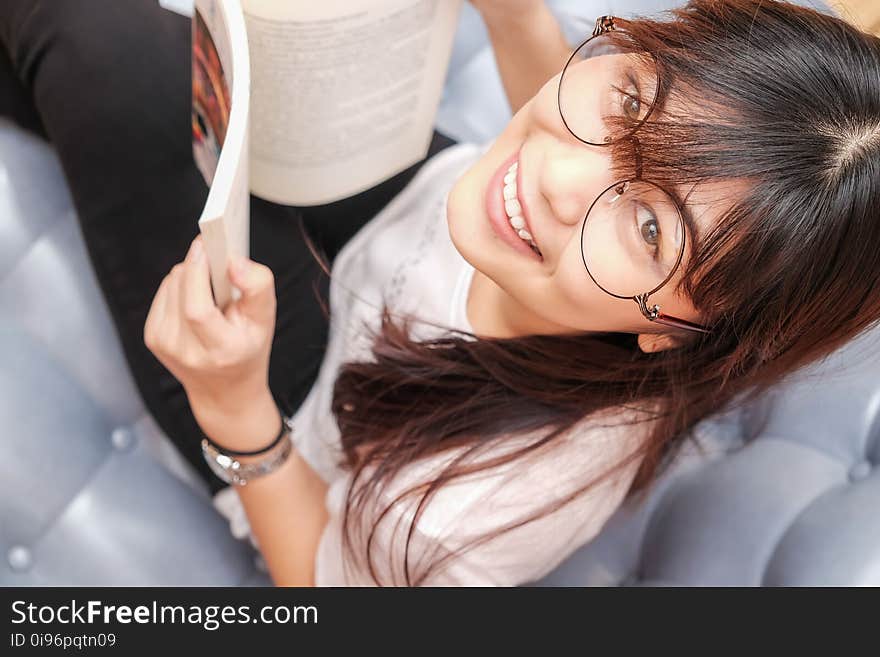 Women wear glasses reading book on cozy sofa smiling