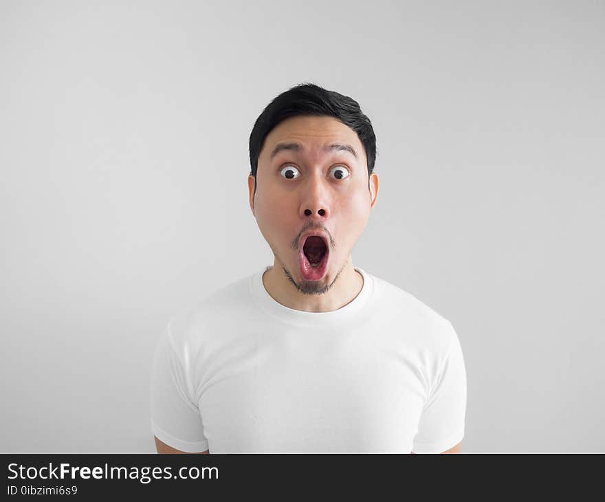 Shocked face of Asian man in white shirt on grey background.