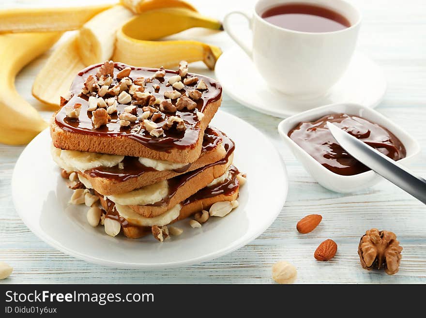 Toasts bread with bananas, walnuts and chocolate on white wooden table