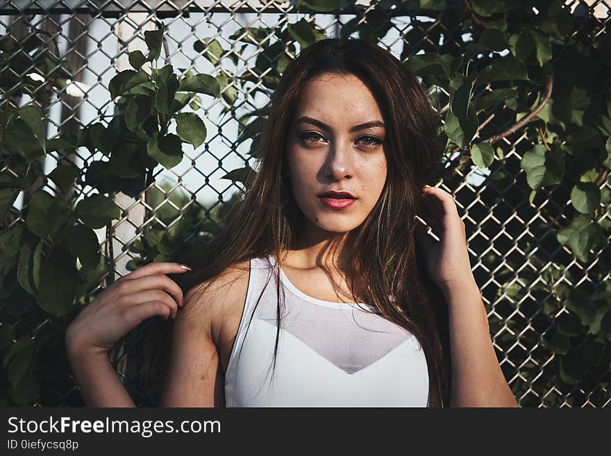 Woman in White Tank Top Standing Near Gray Metal Wire Fence