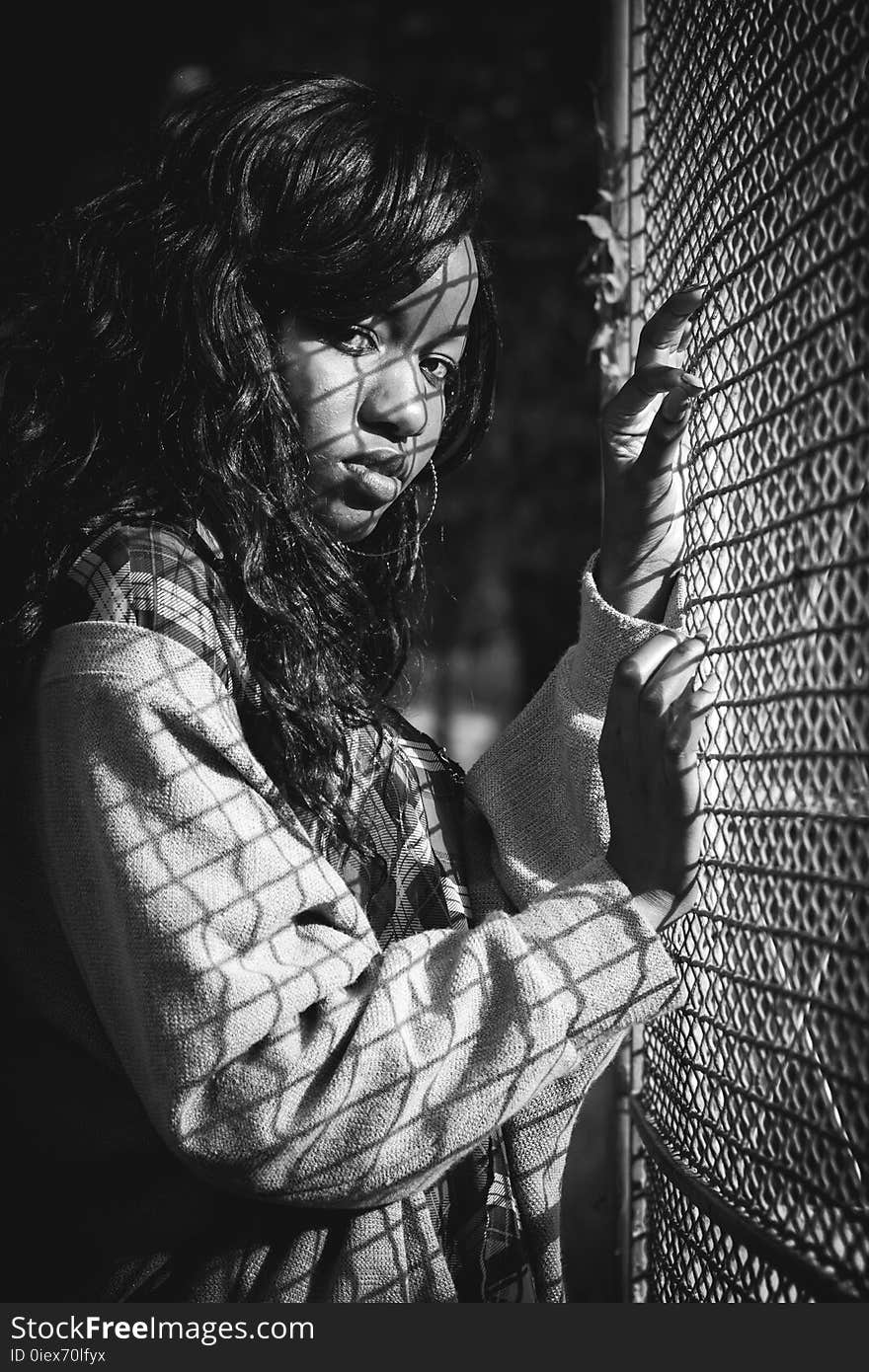 Grey Scale Photography of Woman Standing Against Mesh Grill