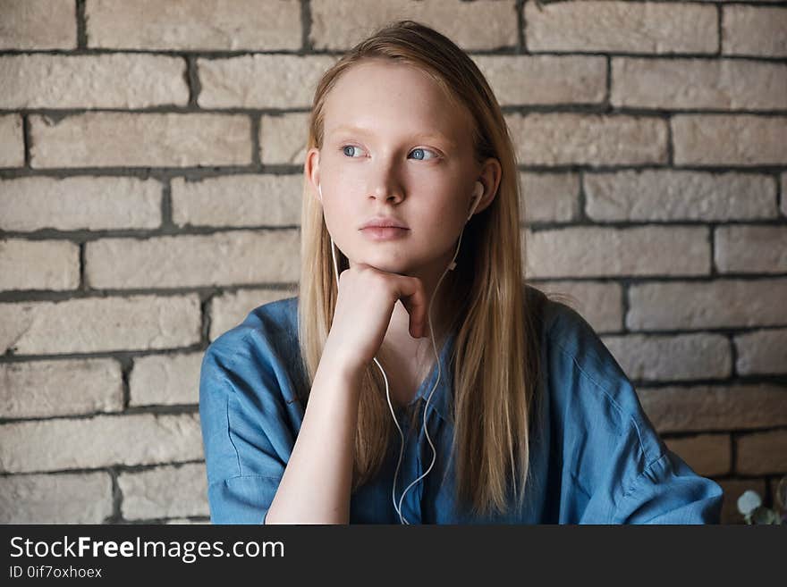 Close up portrait of young blonde girl with headphones. Girls head rests on her hands, On the brick wall background. Close up portrait of young blonde girl with headphones. Girls head rests on her hands, On the brick wall background