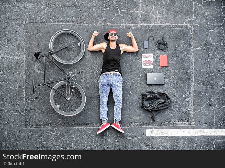 Man in Black Tank Top Laying on Gray Concrete Surface Near Black Bike