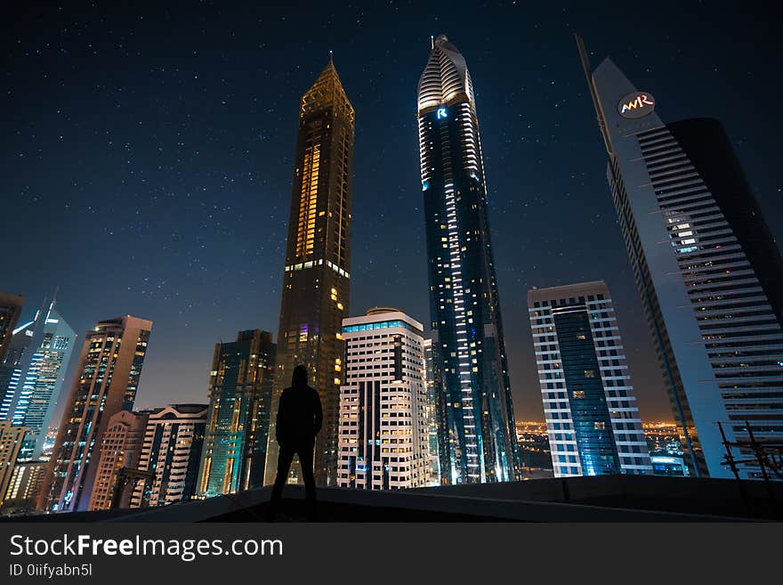 Man Standing in Assorted Building String Light during Night Time