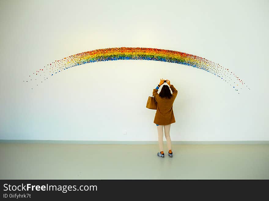 Woman Wearing Brown Top and Beige Leggings Taking Picture Rainbow Painted Wall