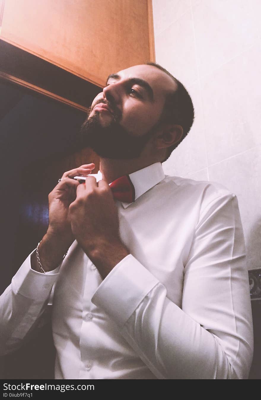 Man in White Dress Shirt Tying a Red Bow Tie