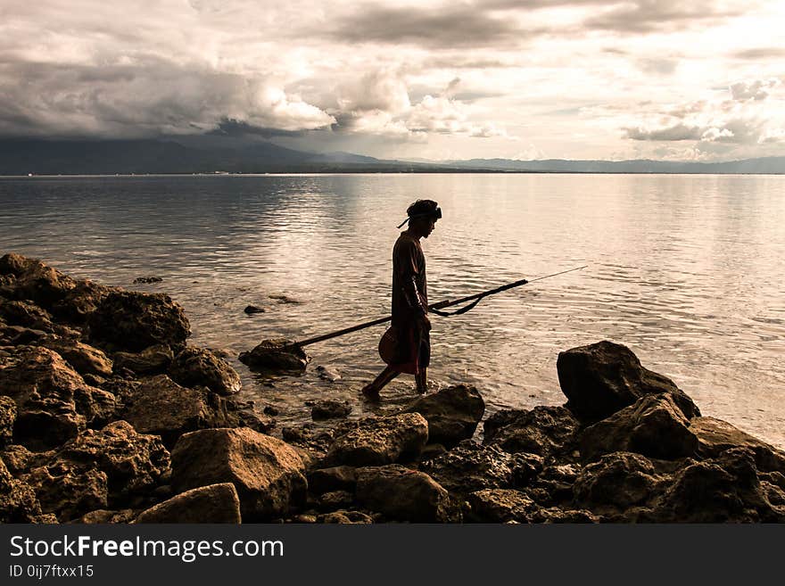 Person Holding Spear Beside Body of Water