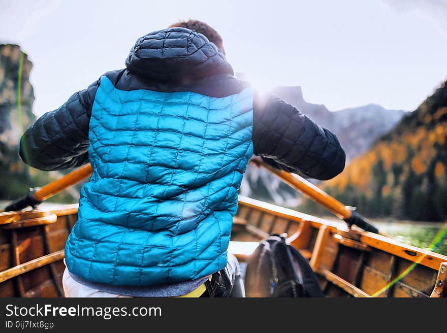 Man in Blue Vest Holding Paddle Sitting Inside Boat