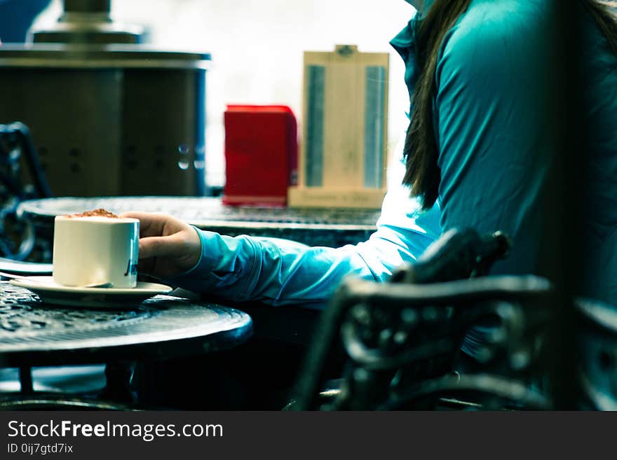 Person in Green Long-sleeved Top Sitting on Chair White Holding White Ceramic Mug