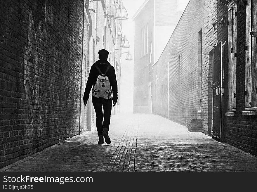 Grayscale Photo of Person Near Brick Wall