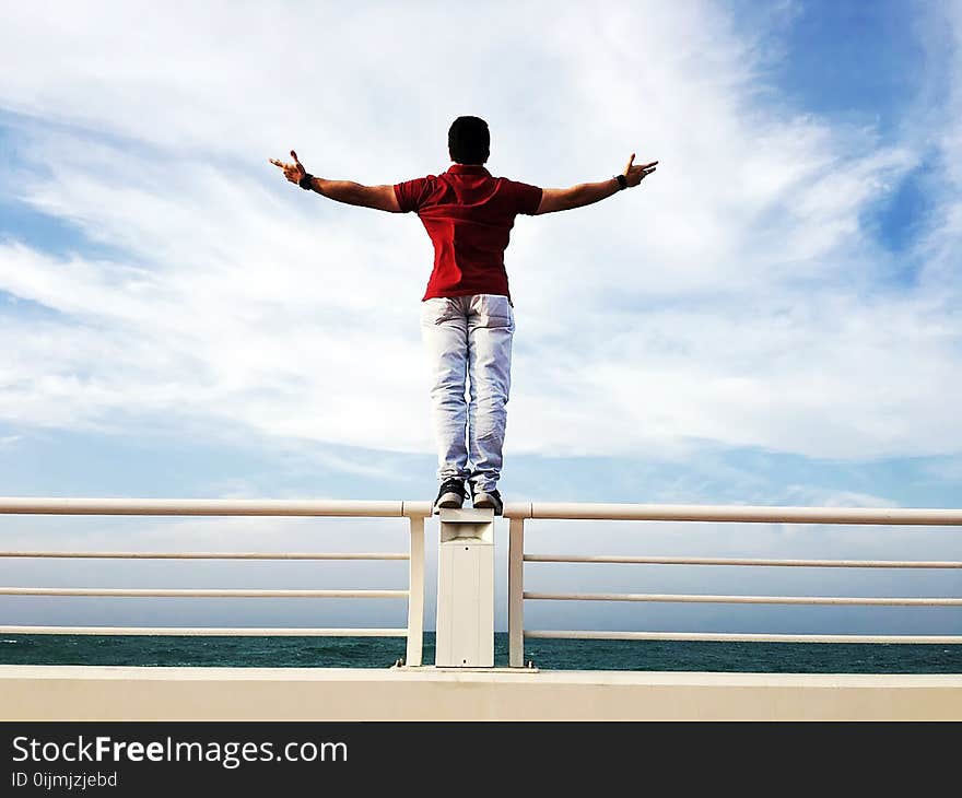 Person Raising Hands Mid-air Sidewards While Standing on Gray Steel Railings