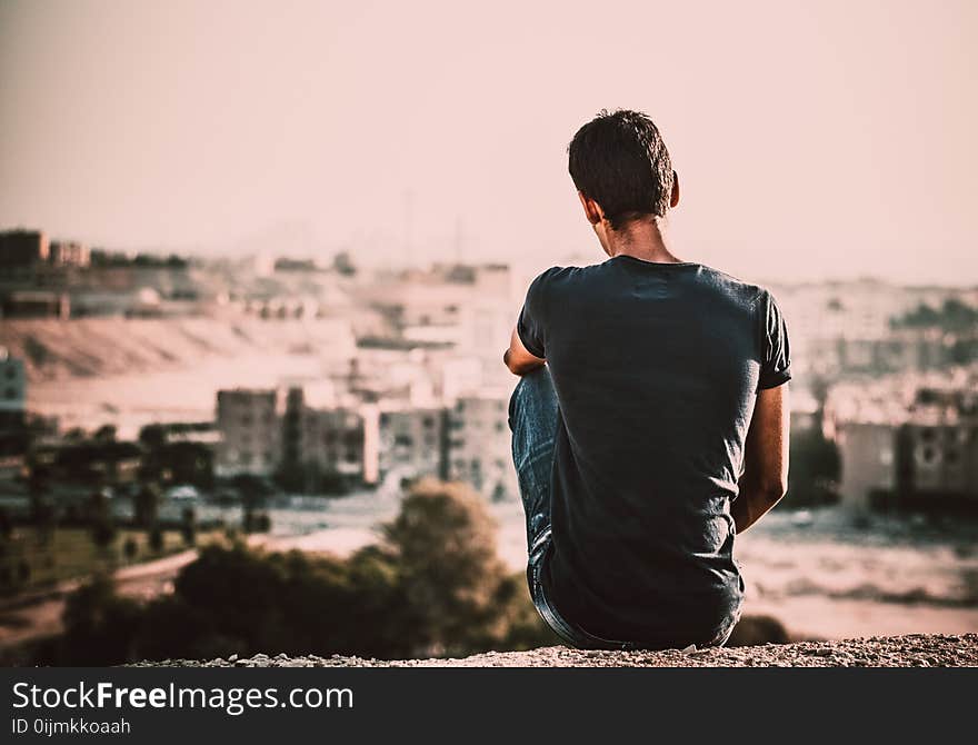 Man in Black Shirt and Blue Denim Jeans Sitting on Gray Stone at Daytime