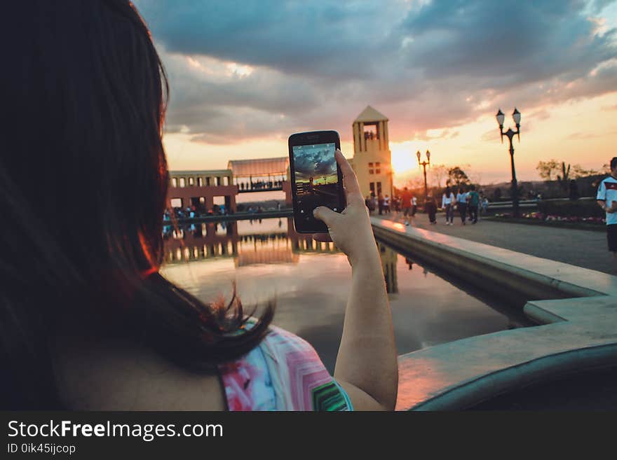 Woman Holding Smartphone Capturing Sunset