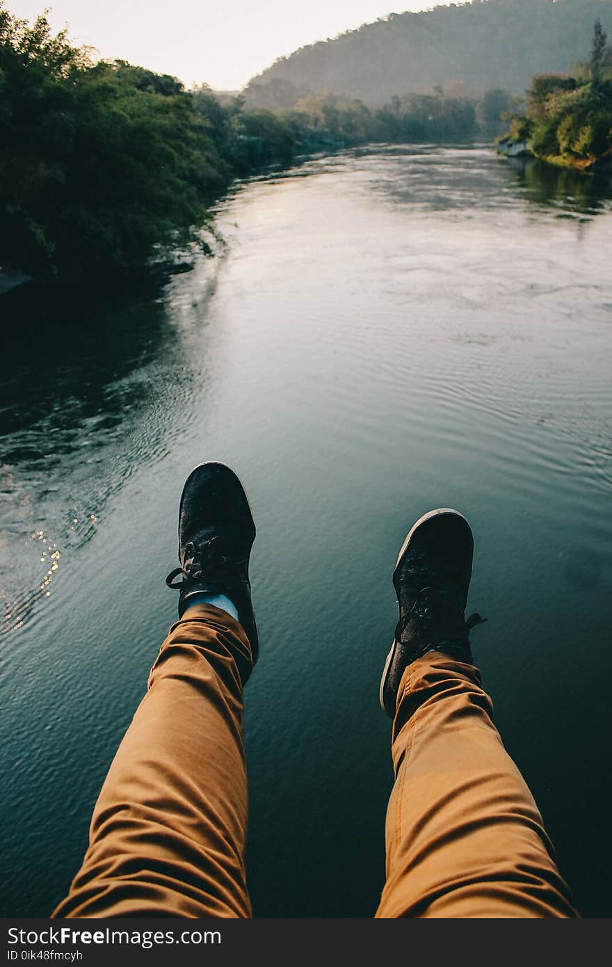 Man in Black Sneakers And Brown Pants Sitting in Front of the River