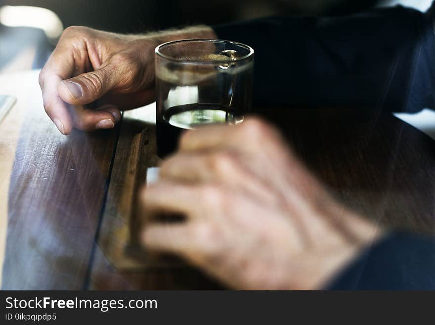 Man in Blue Long Sleeve Shirt In Front Of Drinking Glass On Brown Wooden Table