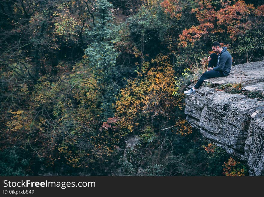 Man In Hoodie Sitting On Rock Cliff