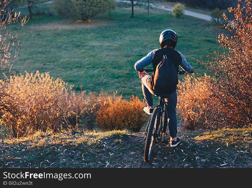 Mountain Biker Stands On The Edge Of A Hill At Sunset Before Rid