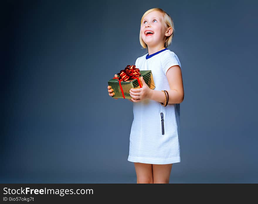 Modern Girl. happy trendy child in white dress isolated on grey background with Christmas present box looking on copy space. Modern Girl. happy trendy child in white dress isolated on grey background with Christmas present box looking on copy space