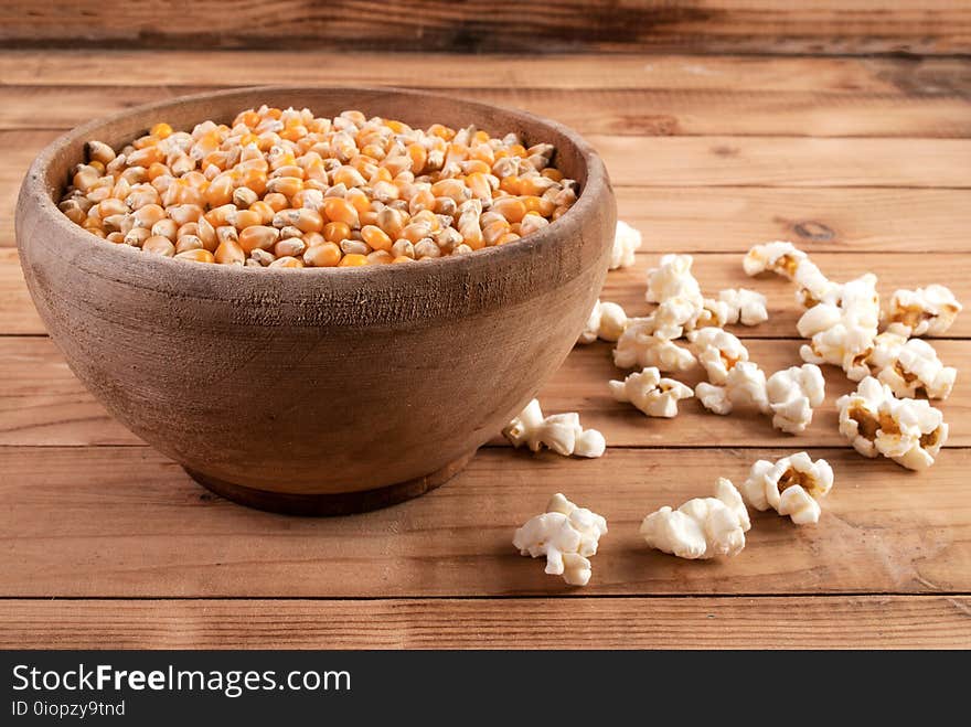 Raw Corn Seeds In Wooden Bowl And Popped Popcorn On Table