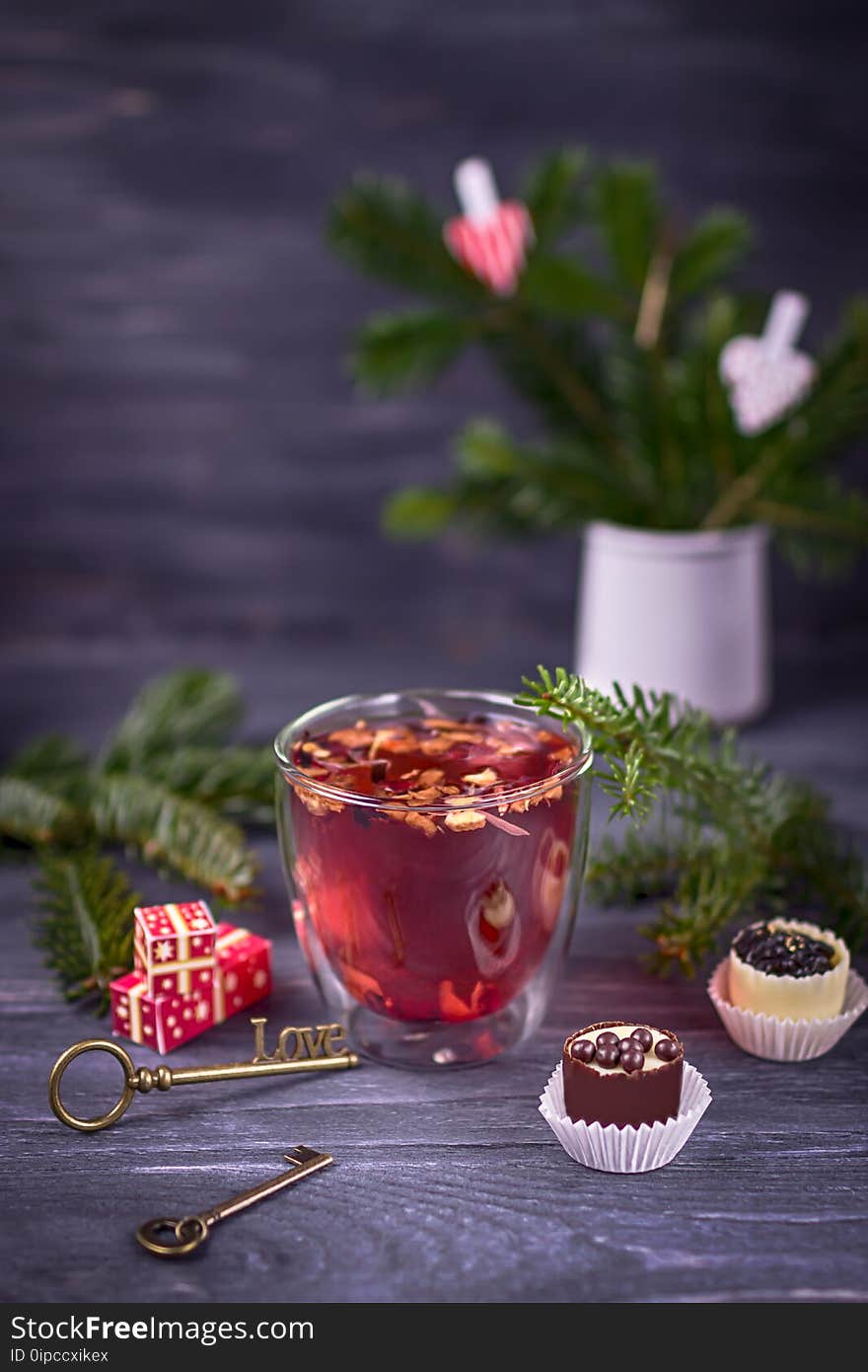 Fruit and hibiscus tea in transparent cup, luxury chocolates candy and christmas tree branch on a dark background