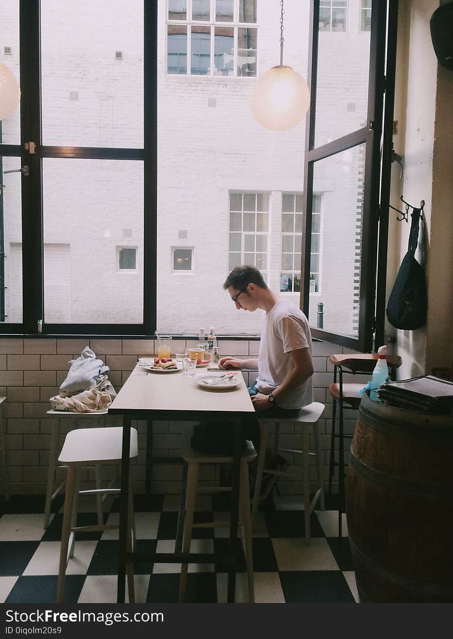 Man Sitting in Front of Table Holding Smartphone Beside Window