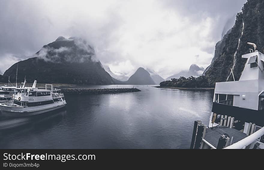 Grayscale Photo of Yachts on Body of Water Under Cloudy Sky