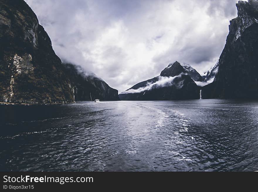 Body of Water Surround by Mountains Under Cloudy Sky