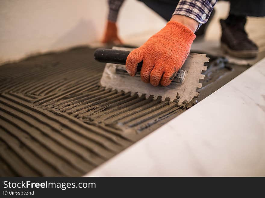 Laying Ceramic Tiles. Troweling mortar onto a concrete floor in preparation for laying white floor tile.