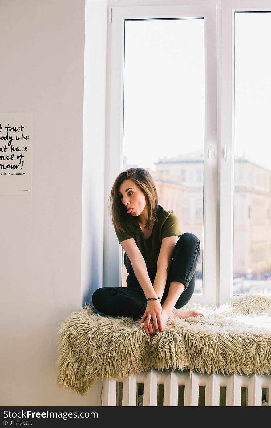 Woman in Green Shirt and Black Denim Jeans Sitting Near Window Inside Room