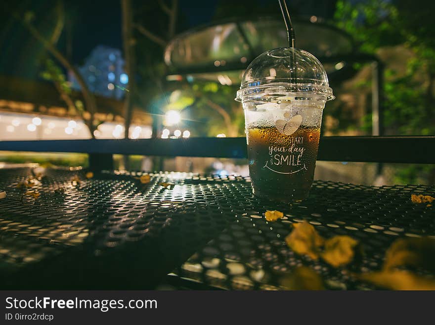 Clear Plastic Disposable Cup With Straw Half-filled With Juice on Metal Table