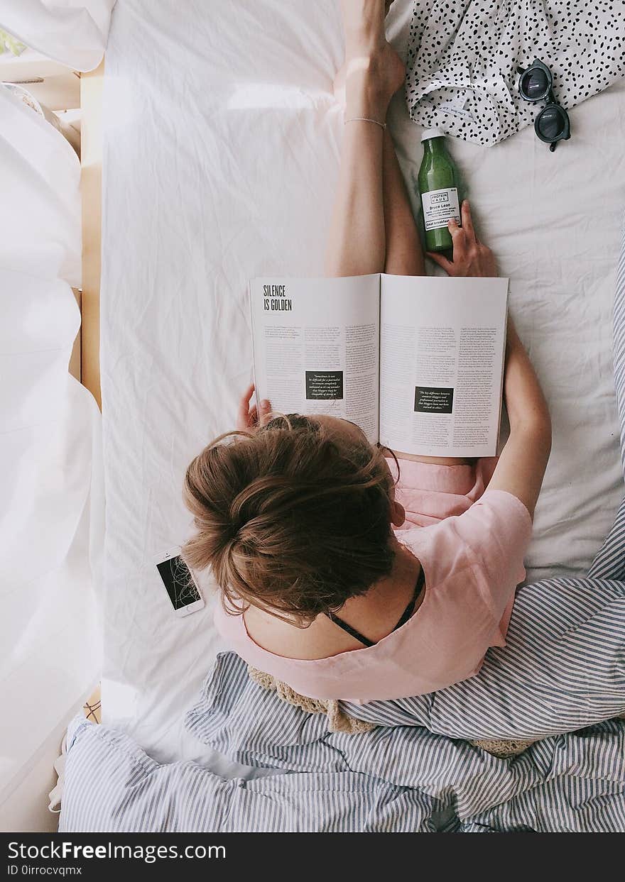 Woman in Pink Dress Sitting on Bed While Reading