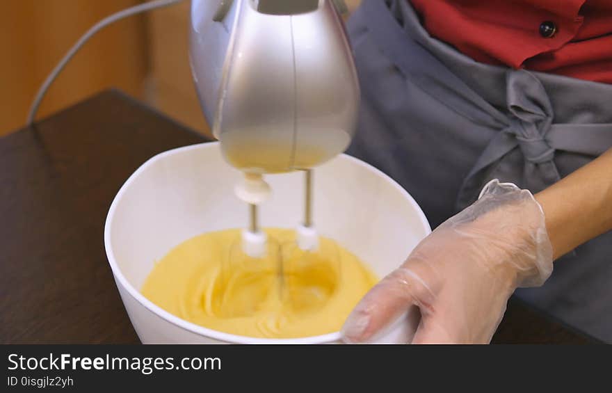 The pastry chef skillfully performs holiday order. A chicken egg is added to the dough. The dough is stirred with a mixer. Woman hand preparing dough and baking a birthday cake. Baking holiday cookies. Christmas and New Year. Magic and dessert for the occasion. The hand of the master in transparent sanitary gloves. 4K 25 h264 Ultra HD