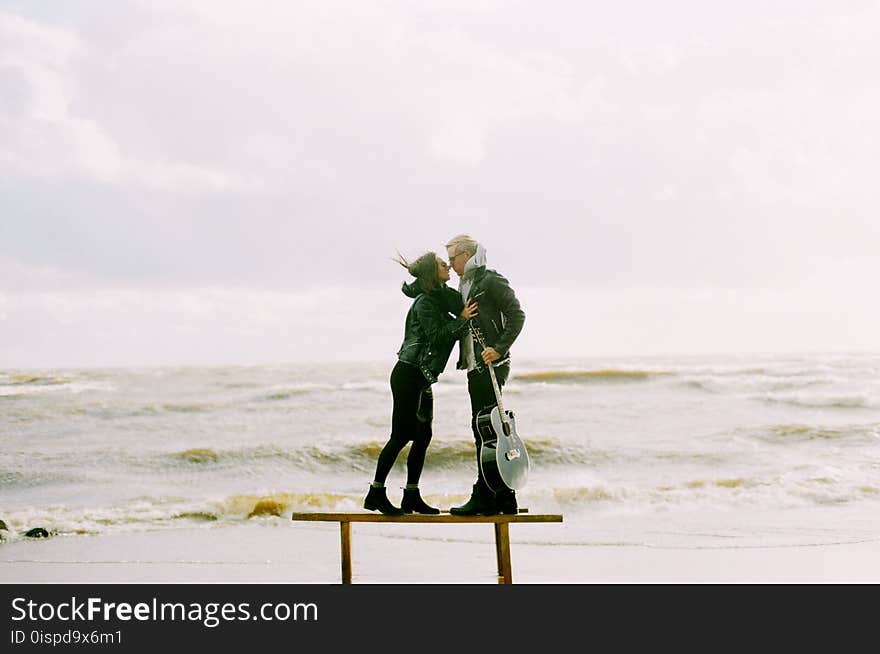 Woman Kissing Man Holding Guitar Beside Beach