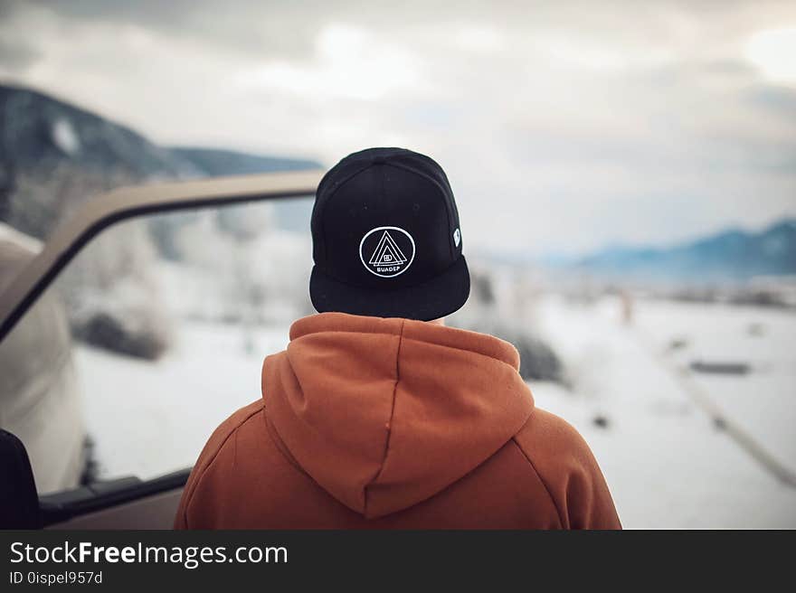 Person Wearing Black Cap and Orange Hoodie Turning His Back