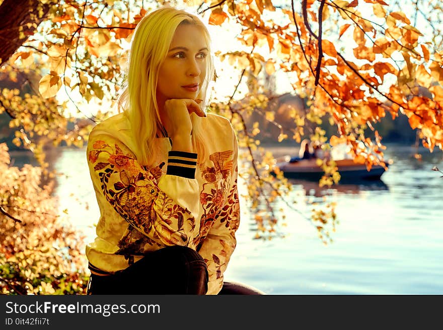 Woman Sitting Under Orange Leaf Tree Near River Bank