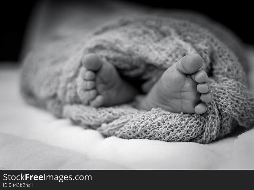 Greyscale Photo Of Human Feet Covered In Knitted Comforter