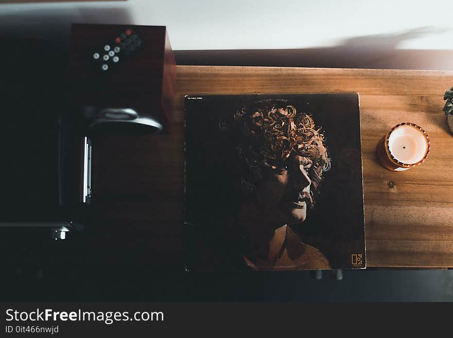 Top View Photography of Vinyl Album Case Near White Tealight Candle Placed on Brown Table