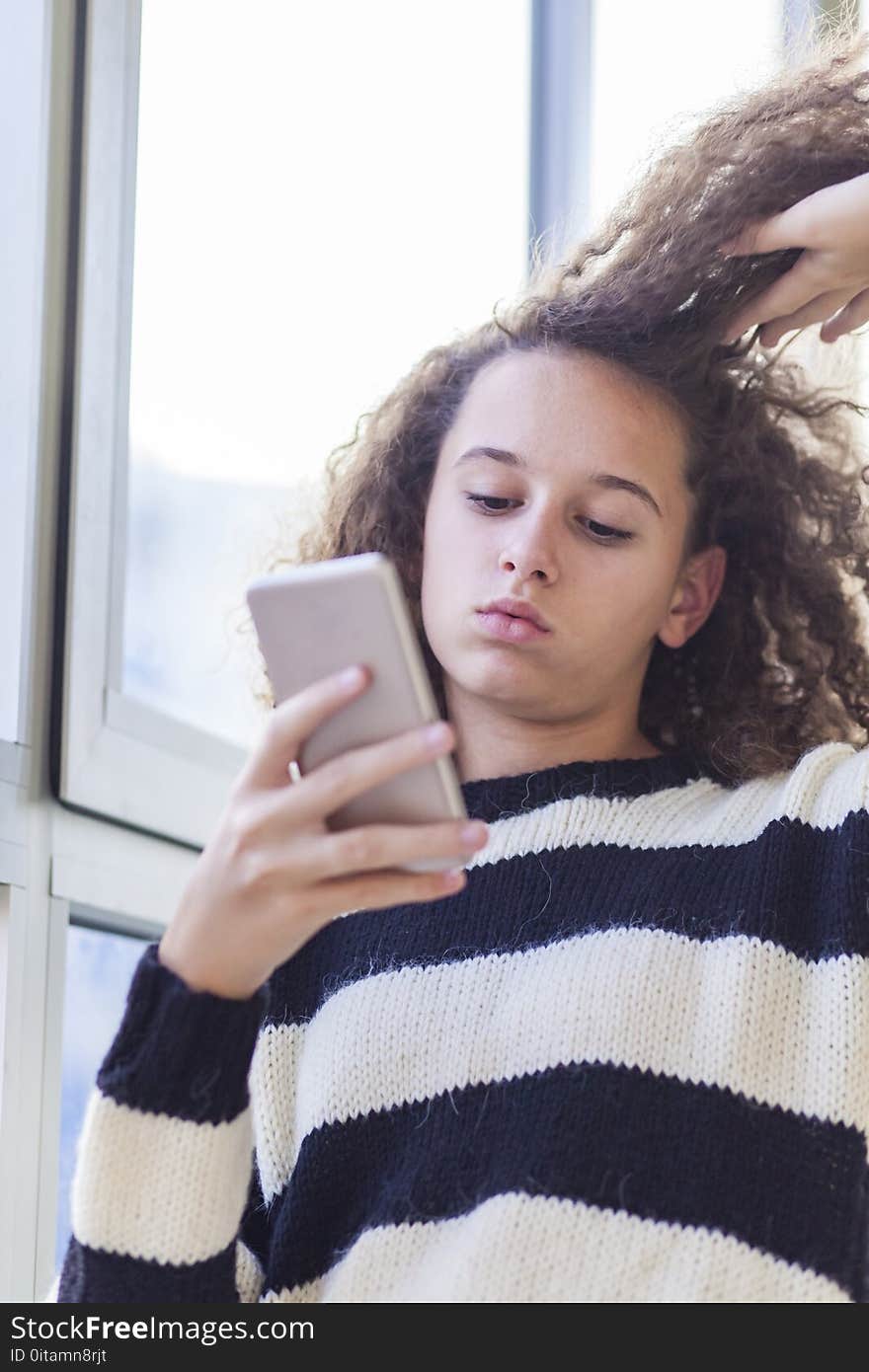 Portrait of curly hair teen girl with mobile phone by window