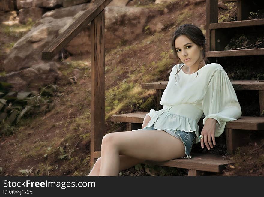 Woman Wearing White Long Sleeve Shirt Sitting on Brown Wooden Stairs