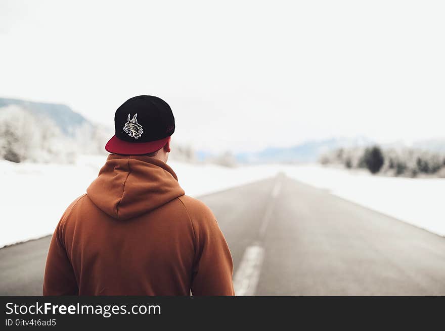 Person in Brown Hoodie and Fitted Cap Walking on Road