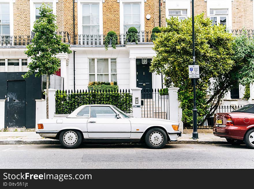 White Coupe Near Brown and White Concrete Building