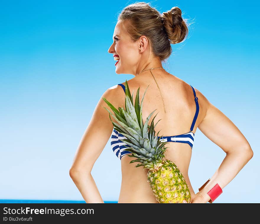 Young woman in bikini on seacoast with pineapple