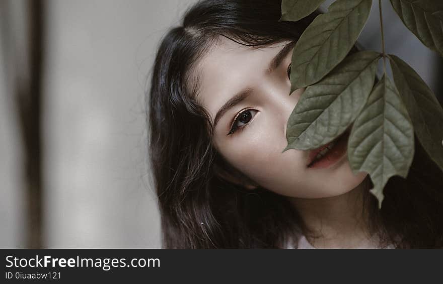 Woman With Black Hair Peeking Through Green Leaves