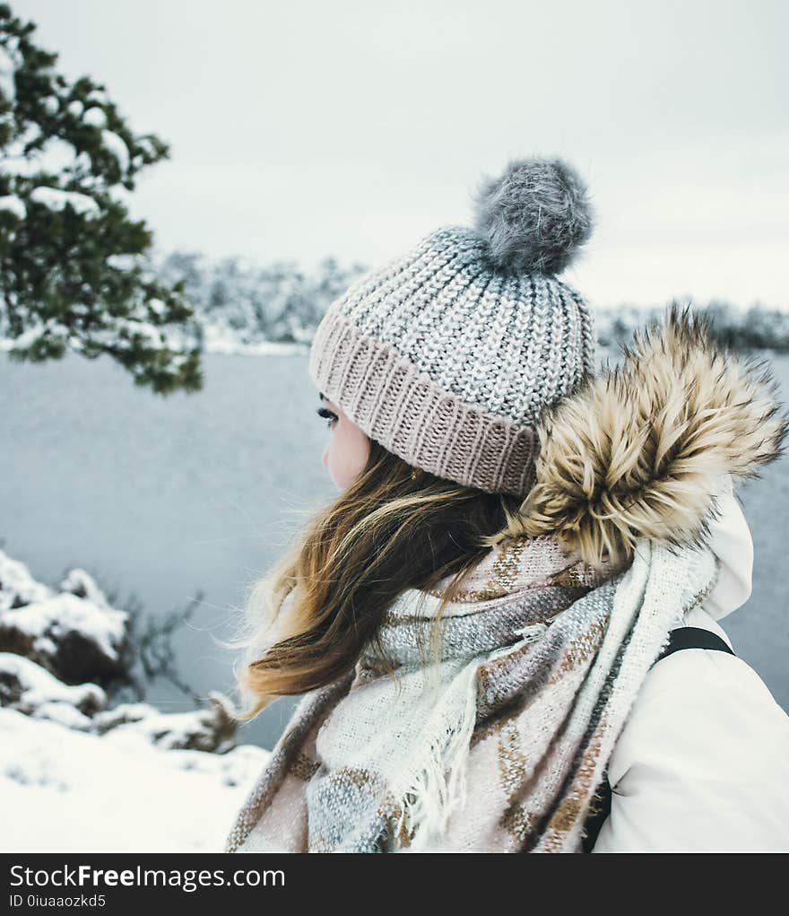 Woman in White and Brown Parka Jacket Wearing Grey Knitted Bobble Hat Near Blue Sea Under White Sky