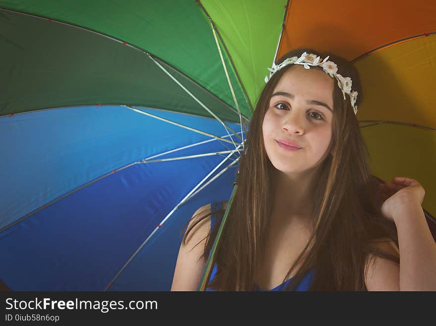 A nice little girl with daisy crown is holding a colored umbrella. A nice little girl with daisy crown is holding a colored umbrella