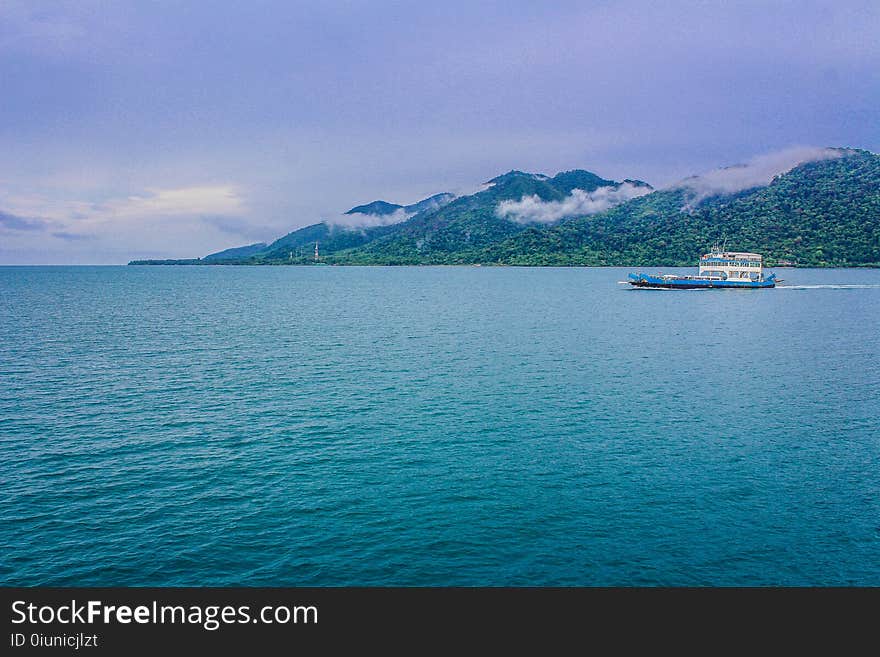 Blue and White Yacht on Teal Sea Near Green Mountain